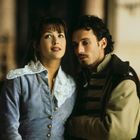 Keine erkennbaren Texte. Eine Frau und ein Mann in historischen Kostümen, eng beieinander stehend in einem Gebäude.