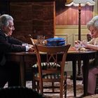 Zwei ältere Personen sitzen sich an einem Esstisch gegenüber. Zwischen ihnen steht ein blauer Topf.