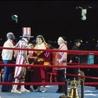 Zwei Boxer stehen sich im Ring gegenüber, umgeben von Trainern und Schiedsrichtern. Einer trägt einen USA-Hut.