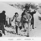 Brigitte Bardot in "PLEASE, NOT NOW". Menschen laufen fröhlich durch den Schnee, Berge sind im Hintergrund zu sehen.