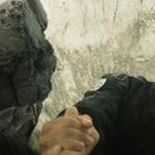 Person mit Uniform hält Hand. Namensschild zeigt "R. Garcia". Hintergrund aus Felsen und Staub. Gesicht angestrengt.