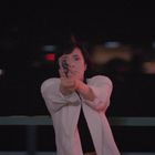 Keine Texte sichtbar. Eine Person in heller Kleidung zielt fokussiert mit einer Pistole im Dunkeln.