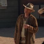 Eine Person in altwestlicher Kleidung steht draußen vor einer Wand mit Steckbriefen.