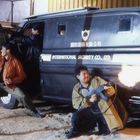 „INTERNATIONAL SECURITY CO., LTD.“ steht auf einem schwarzen Transporter. Drei Männer feuern Waffen ab.