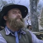 Keine erkennbaren Texte. Ein bärtiger Mann mit Hut steht mit geschlossenen Augen; Menschenmenge im Hintergrund.