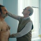 © zeigt eine Untersuchung in einem Arztzimmer. Ein Mann wird von einem älteren Mann vermessen. Ein Anatomieposter an der Wand.