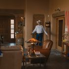 Roter Schriftzug an der Wand: "NO JUSTICE". Zwei Polizisten in Uniform, ein Mann mit Cowboyhut im Hintergrund. Wohnzimmer.