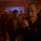 Ein Sheriff mit Funkgerät steht vorne, Menschen mit Winterkleidung im Hintergrund einer gemütlichen Bar.