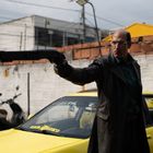 Text "Kamikoku" auf der Frontscheibe eines gelben Autos. Ein Mann in Ledermantel zielt mit einer Schrotflinte.