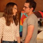 Zwei Personen stehen sich in einer Wohnung gegenüber. Der Mann trägt Brille und graues Shirt, die Frau ein Hemd mit roten Mustern.