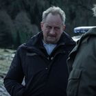 Ein Mann in Gendarmerie-Uniform spricht mit zwei Personen vor einer winterlichen Waldkulisse.