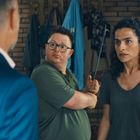 Es gibt keine sichtbaren Texte. Drei Personen stehen in einem Raum, eine davon trägt einen blauen Anzug.