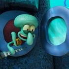 Eine Zeichentrickfigur mit Tentakeln schaut aus einem runden Fenster. Sie hält eine Klarinette in der Hand.