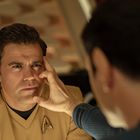 Ein Mann in einer beigen Uniform mit einem Stern-Logo wird von einer Hand an der Schläfe berührt. Im Hintergrund unscharf.