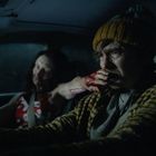 Ein Mann mit gelber Mütze sitzt im Auto, erschrocken. Eine Person mit blutigen Händen ist neben ihm. Atmosphärisch dunkel.