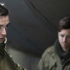 Drei Männer in Winterkleidung stehen in einem Zelt. Der linke Mann trägt eine Militärjacke mit Abzeichen.