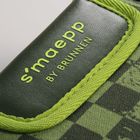 Text: "s'maepp BY BRUNNEN". Grünes textile Umsäumung auf karierter, dunkelgrüner Oberfläche.