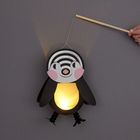 Ein leuchtender Laternenpinguin mit spiralförmigem Muster am Kopf, gehalten von einem Stock, strahlt sanftes gelbes Licht aus.