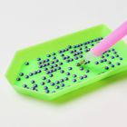 Grünes Tablett mit lilafarbenen runden Perlen, daneben ein pinkfarbener Stift mit Metallspitze.