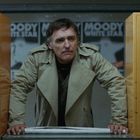 Texte: "Fahrscheine", "MOODY", "WHITE STAR". Mann in beigefarbenem Trenchcoat zwischen gelben Automaten.