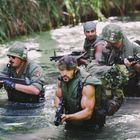 Ich kann den Text im Bild nicht beschreiben. Vier Männer in Militärkleidung waten durch einen dichten, bewachsenen Fluss.
