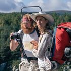 „NORGES FJELLHEIMER“ steht auf einem Shirt. Zwei Personen im Wald, eine mit Kamera, die andere mit großem roten Rucksack.