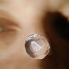 Keine erkennbaren Texte. Ein Wassertropfen schwebt vor einem unscharfen Hintergrund mit menschlichen Augen.