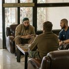 Text: "PULL". Drei Männer sitzen auf Ledersesseln um einen Tisch. Einer trägt ein langes Gewand und eine Mütze.