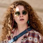 Ich kann keine Texte oder Logos erkennen. Eine Frau mit Locken, Sonnenbrille und kariertem Hemd, draußen stehend.