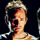 Ich kann die Texte im Bild nicht sehen. Ein Mann mit einem ernsten Gesichtsausdruck in dunkler Umgebung.