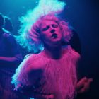 Ich kann keine Texte erkennen. Eine Person tanzt leidenschaftlich in buntem Licht mit ausdrucksstarkem Gesicht.