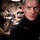 Zwei Personen in dunkler Kleidung, eine mit einer futuristischen Waffe. Die Atmosphäre ist angespannt, wie in einem Keller.