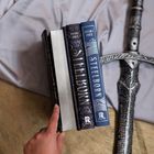 Zwei Bücher mit "Steelborn" auf dem Rücken, daneben ein Schwert und eine Hand mit ausgestrecktem Finger.