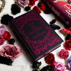 „MAKE ME YOUR INSTRUMENT OF VENGEANCE“ in rosa auf schwarzem Buch. Umgeben von bunt gefärbten Blumen.