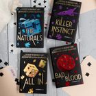 Vier Buchcover von Jennifer Lynn Barnes liegen auf einem Tisch mit Puzzlestücken und Spielkarten.