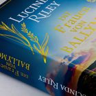 „DIE FRAUEN VON BALLYMORE“ von Lucinda Riley, umgeben von Gebirgslandschaft und blauem Himmel.