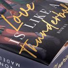 "Love is like a Thunderbolt" steht auf einem Buchcover, darüber eine Illustration von sich haltenden Händen.