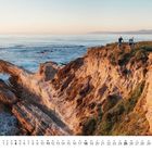 Kalenderseite für Juli, zeigt zwei Radfahrer auf einer felsigen Klippe am Meer bei Sonnenuntergang.