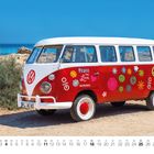 "Peace and Love" steht auf einem bunten VW-Bus mit Blumenmustern, auf einem sandigen Küstenweg.