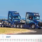 Text: "JULI", "2027", "Inge Bings", "VALHALLA". Zwei blau lackierte Lastwagen mit künstlerischen Designs auf einer Rennstrecke.