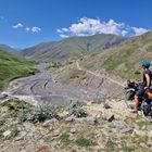 Ein Radfahrer mit Helm steht auf einem Hügel und schaut über ein grünes Tal mit einem schlammigen Fluss.