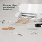 „Kreative Ideen professionell umsetzen“; Tisch mit Schneideplotter, Schere, Kartonstücken, Werkzeugen verteilt.