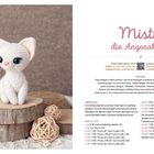 "Misty, die Angorakatze" Anleitung in rosa Schrift. Links: Häkelkatze auf Holzscheiben, umgeben von dekorativen Kugeln.