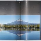 Ein offenes Buch zeigt eine beeindruckende Aussicht auf einen Berg, der sich in einem stillen Gewässer spiegelt.
