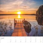 Text: "Juli", Wochentage und Kalendertage. Ein Steg führt zu einem ruhigen See, Boot daneben, Sonnenuntergang im Hintergrund.