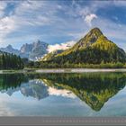07 | JULI. Malerische Berglandschaft mit einem klaren See im Vordergrund, in dem sich die Berge spiegeln.
