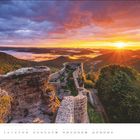 Text: "Juli". Ein Sonnenaufgang über einer Landschaft mit alten Mauern und dicht bewaldeten Hügeln.