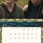 Kalenderseite für Juli, Montag bis Sonntag mit einem kleinen, fliegenden Drachen unten. Zwei lächelnde Personen oben.