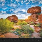07. Unter einem klaren blauen Himmel ragen große, rötliche Felsen hervor, umgeben von grüner Vegetation.