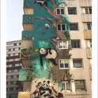 Wandgemälde: Zwei Pandas im Baum, ein weiterer mit zwei Personen unten. Text (Französisch): "Ici rien que..."